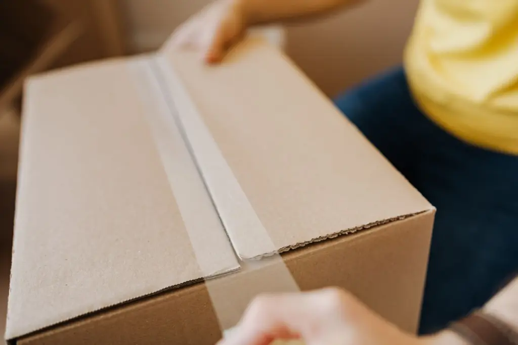Manos precintando una caja de cartón con cinta adhesiva