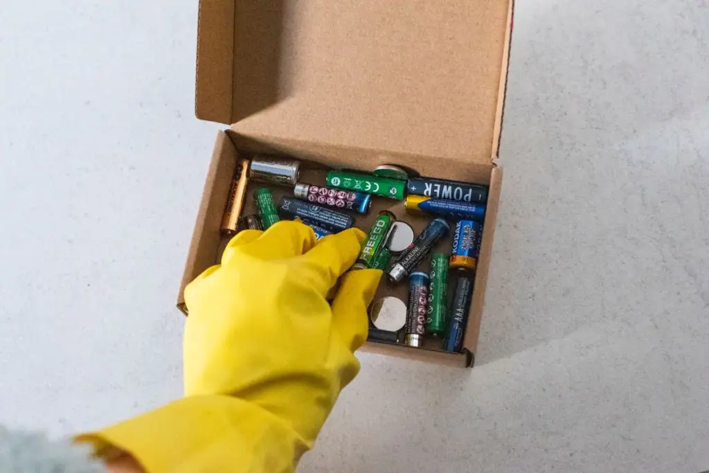 Mano con guante recogiendo pilas usadas en una caja para reciclarlas