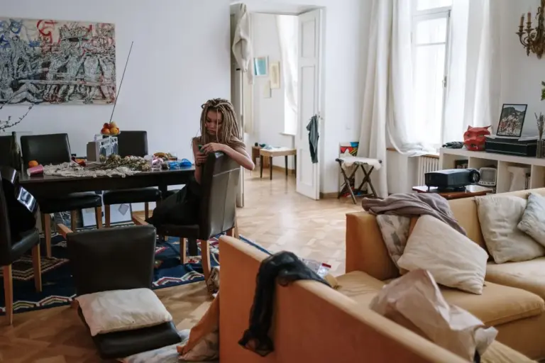 Salón desordenado con ropa y cojines sobre el sofá y la mesa llena de objetos